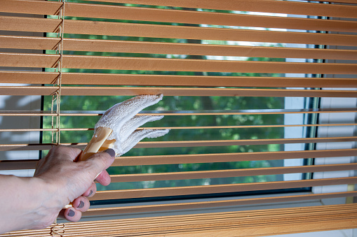 a woman's hand cleans wooden blinds