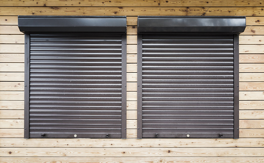 Wooden wall with two windows protected with roller shutters, background texture