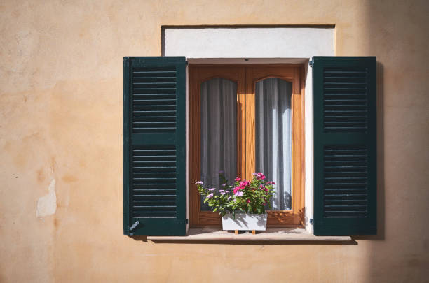 Window with open shutters and flowers at sunset, color toning applied, Mallorca, Spain.