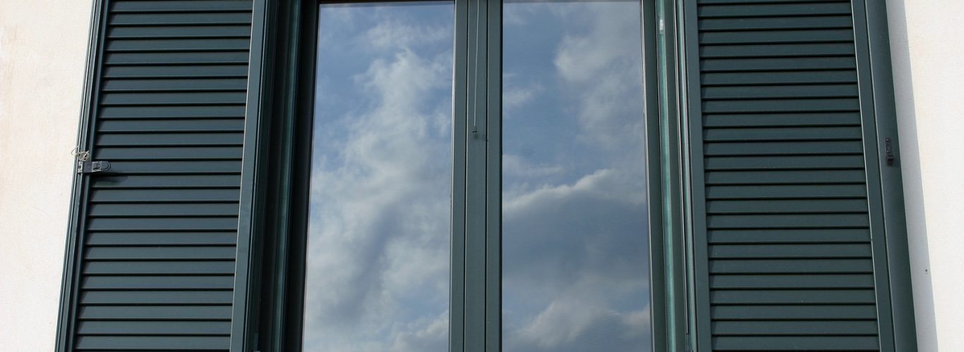Window with open shutters reflecting the sky.