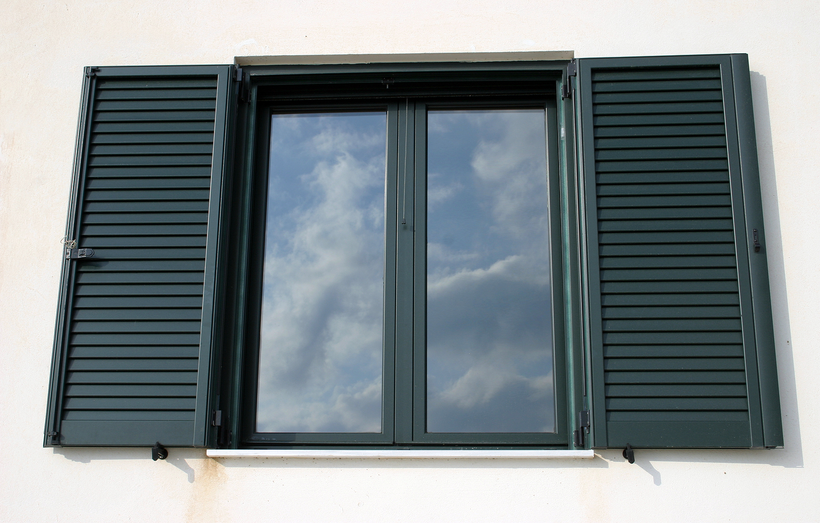 Window with open shutters reflecting the sky.